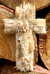 Handgefertigtes florales Kreuz aus cremefarbenen Trockenblumen auf rustikalem Holz